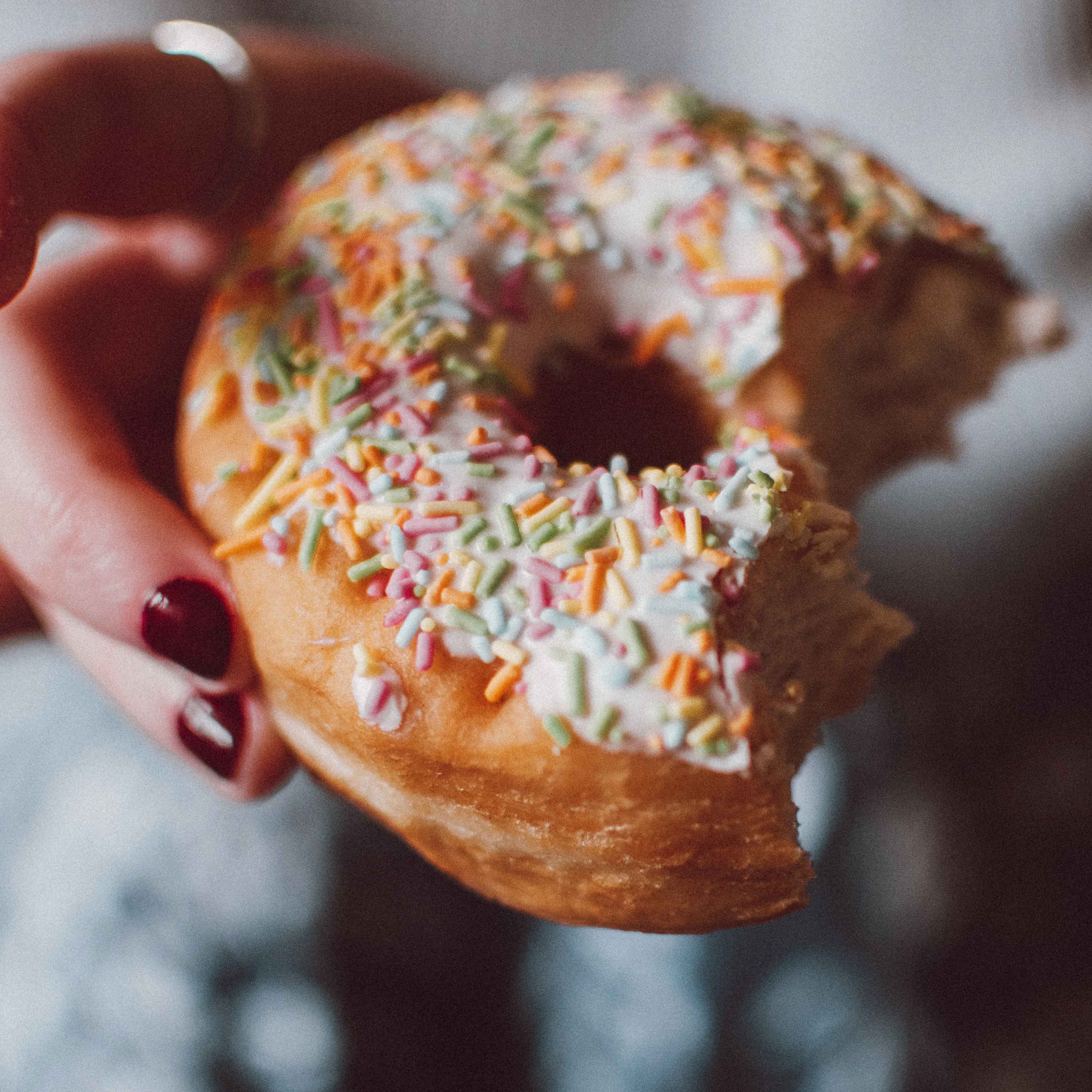 Hand holding a sprinke donut with some bites in it