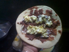 An open homemade baleada with eggs, butter, cheese and beans